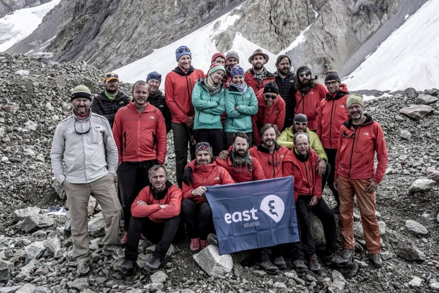 Zespół produkcyjny East Studio pozuje z flagą firmy na tle ośnieżonych gór podczas realizacji zdjęć do filmu Broad Peak w Karakorum.