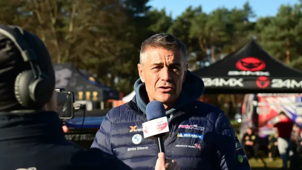 Krzysztof Hołowczyc udziela wywiadu. Stoi w puchowej kurtce przed dziennikarzem, który wystawia mu mikrofon