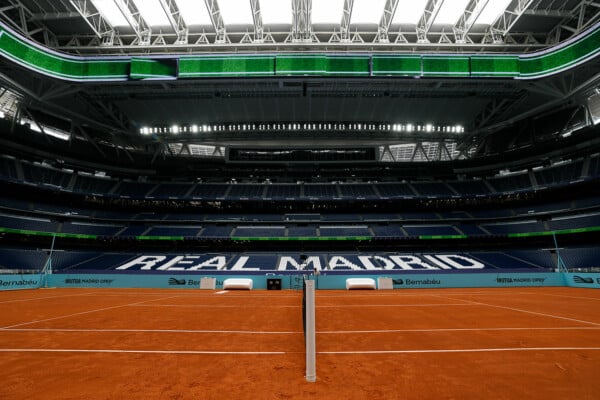 Widok na ceglany kort tenisowy zainstalowany na murawie stadionu Santiago Bernabéu w Madrycie z widocznym napisem Real Madrid na trybunach.