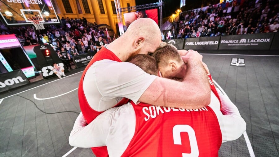 Trzej polscy koszykarze w czerwonych strojach reprezentacji cieszą się i ściskają na boisku po wygranym meczu koszykówki 3x3.