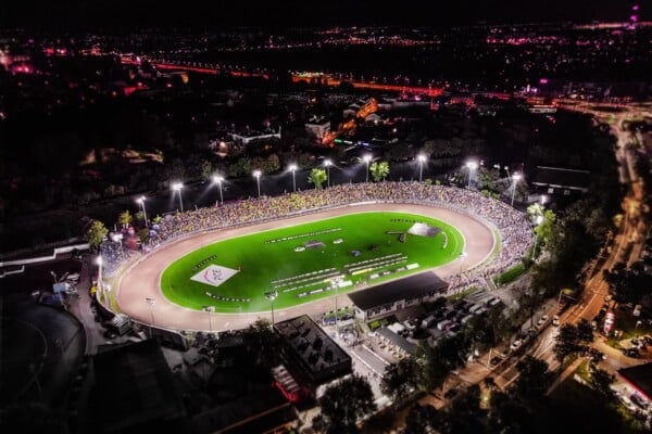 Widok z góry na oświetlony stadion żużlowy w Lublinie w nocy, pełne trybuny kibiców, zawodnicy na torze, logo PGE na trawie.