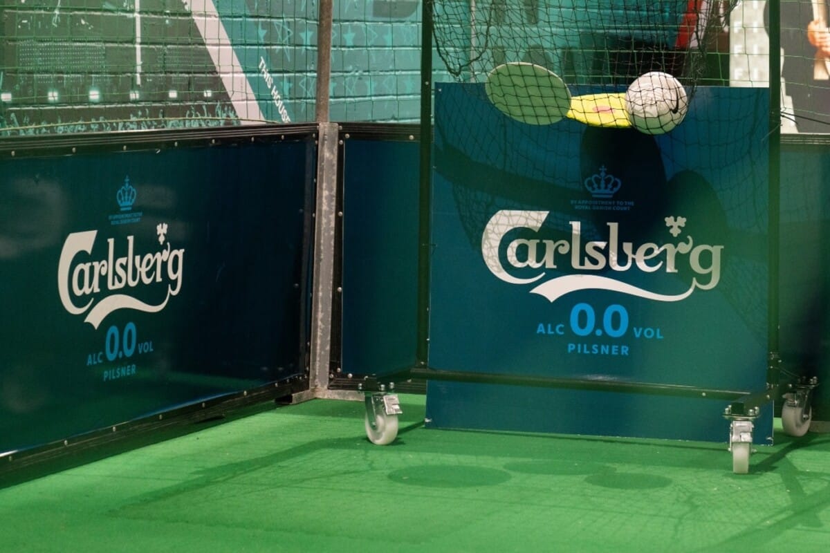 Brandowane bandy i tablice reklamowe piwa bezalkoholowego Carlsberg 0.0 Pilsner podczas sportowej aktywacji dla kibiców na boisku piłkarskim.