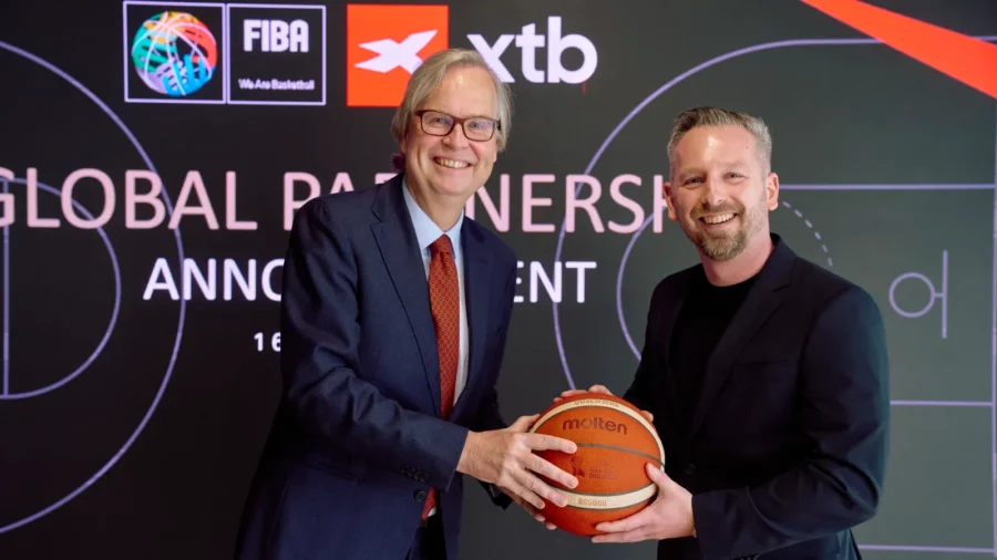 Ogłoszenie globalnego partnerstwa FIBA i XTB: przedstawiciele obu organizacji uśmiechają się, trzymając wspólnie piłkę do koszykówki marki Molten na tle ścianki z logotypami.
