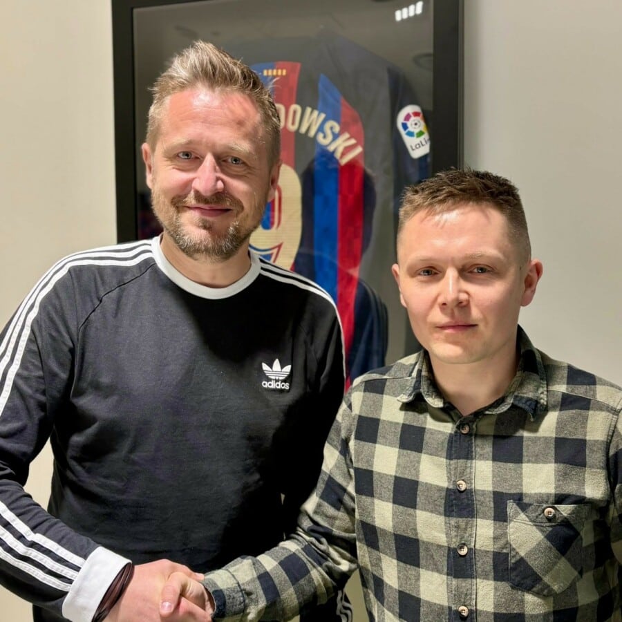 Michał Kołodziejczyk i Tomasz Ćwiąkała ściskają sobie dłonie na tle oprawionej koszulki FC Barcelona.