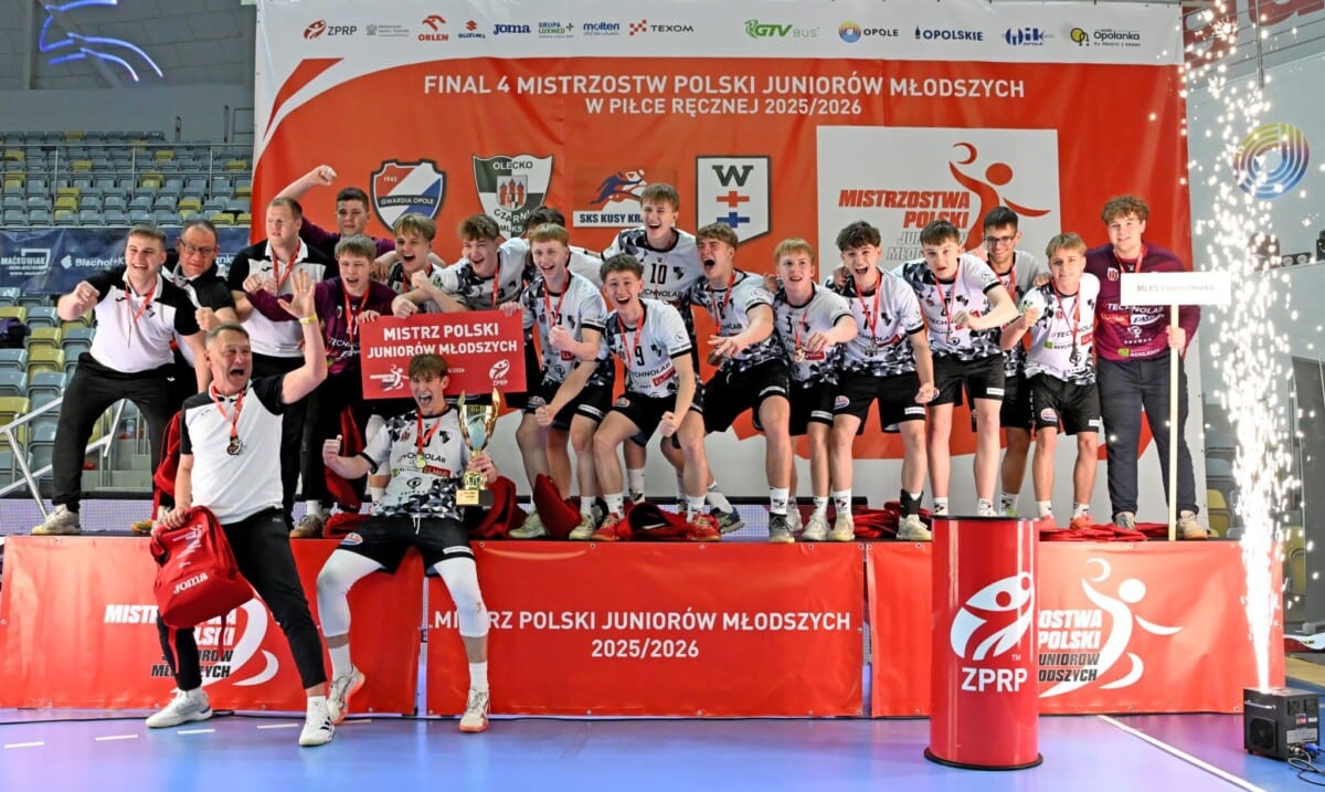 Młodzi piłkarze ręczni świętują zdobycie tytułu Mistrza Polski Juniorów Młodszych 2025/2026 na podium ZPRP, trzymając puchar i pamiątkową tablicę.