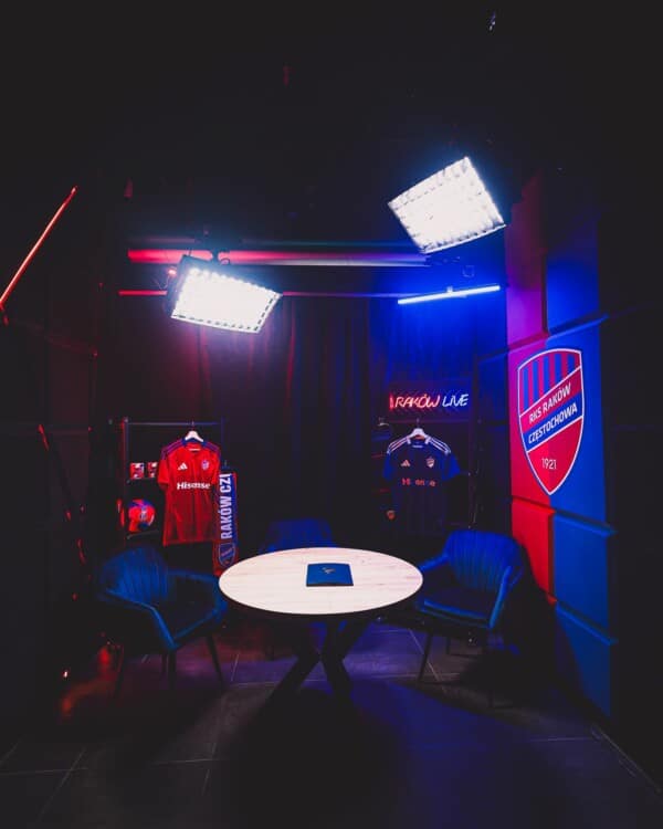 Widok na profesjonalne studio podcastowe Rakowa Częstochowa ze sprzętem Expander Integrator IT, krzesłami, stołem i neonem "RAKÓW LIVE".
