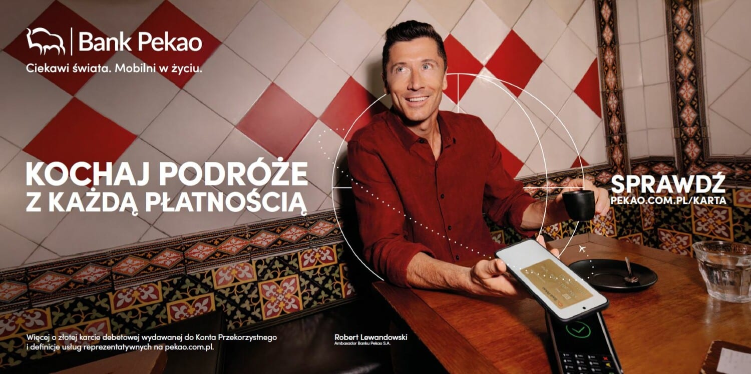Plakat marketingowy Banku Pekao z kampanii „Ciekawi świata. Mobilni w życiu”, na którym ambasador marki Robert Lewandowski wykonuje płatność zbliżeniową telefonem w restauracji.