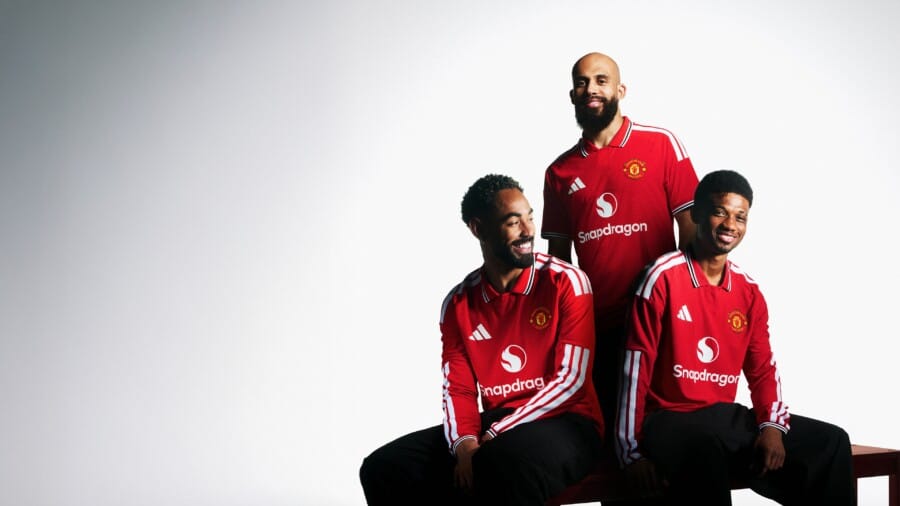 Trzech mężczyzn w czerwonych koszulkach Manchester United Adidas, prezentujących nowy domowy strój piłkarski na sezon 2026/2027 na jasnym tle