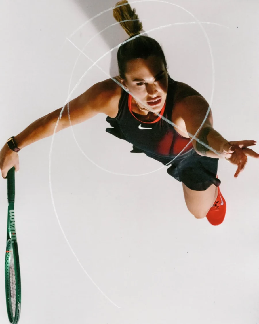 Aryna Sabalenka na białym tle. Zawodniczka pozuje w czerwonym body projektu Nike. Trzyma rakietę tenisową i przygotowuje się do odbicia piłki tenisowej.