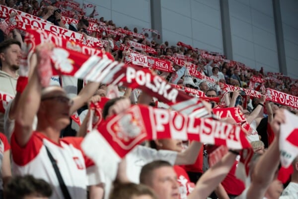 Wypełnione trybuny hali sportowej w Katowicach podczas meczu piłki ręcznej, kibice w biało-czerwonych barwach trzymają uniesione szaliki z napisem "POLSKA".