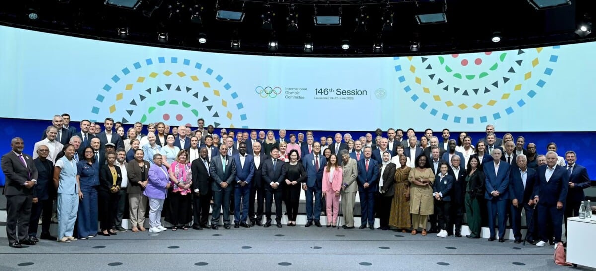 Uczestnicy 146. Sesji Międzynarodowego Komitetu Olimpijskiego w Lozannie stojący wspólnie na scenie na tle wielkiego ekranu z logo MKOl.