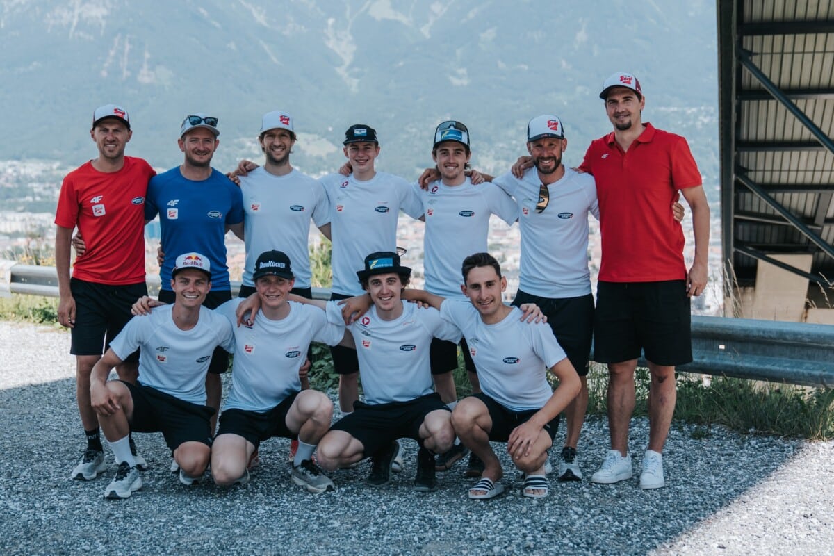 Reprezentacja Ski Austria w kombinacji norweskiej pozuje do wspólnego zdjęcia w letnich strojach sportowych marki 4F na tle gór.
