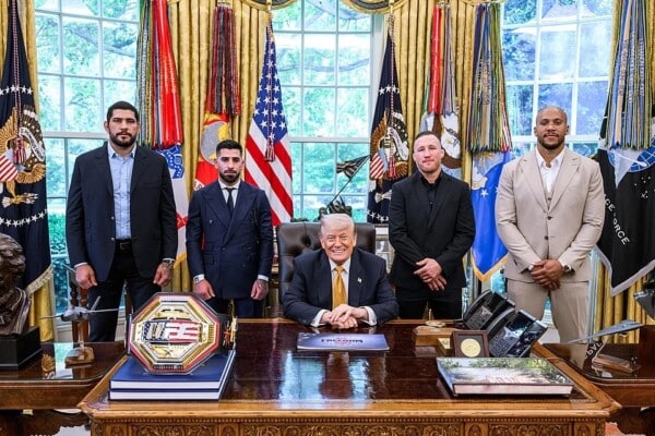 Donald Trump siedzący przy biurku w Gabinecie Owalnym z zawodnikami UFC stojącymi obok podczas spotkania w Białym Domu.