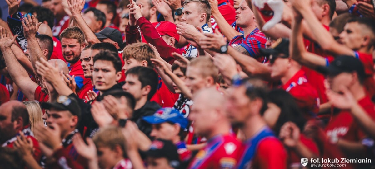 Tłum kibiców Rakowa Częstochowa w czerwono-niebieskich barwach klubowych klaszcze i dopinguje swoją drużynę na trybunach stadionu podczas meczu.