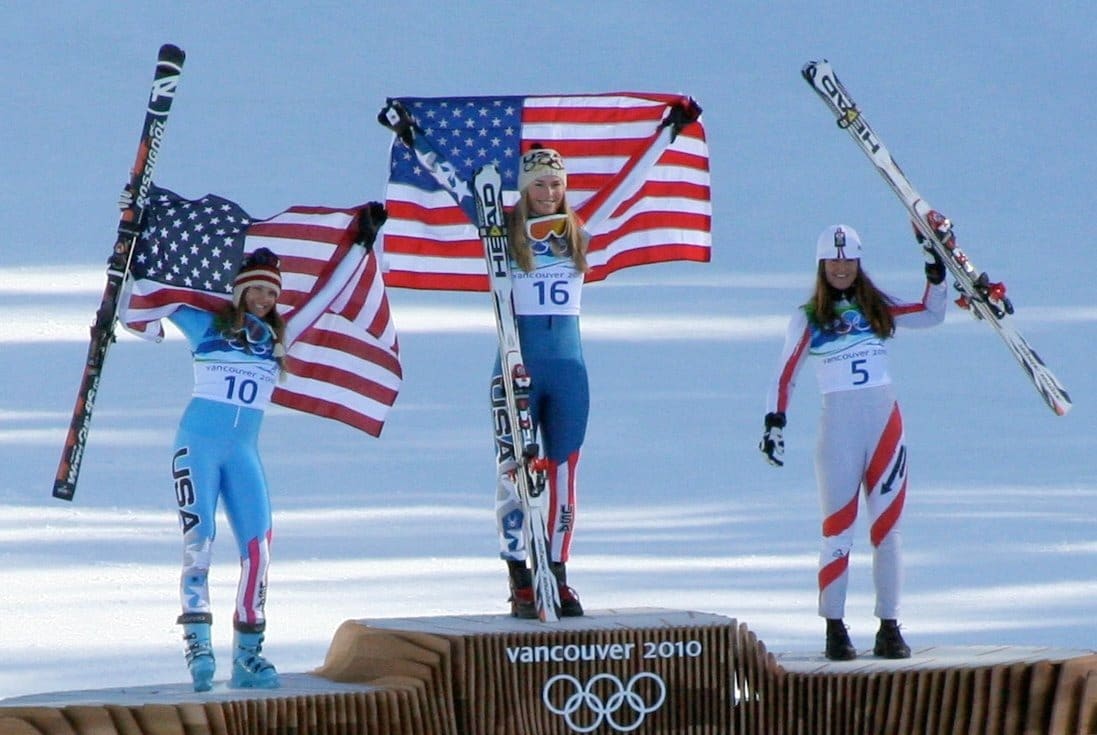 Trzy medalistki kobiet w zjeździe narciarskim na podium podczas zimowych igrzysk olimpijskich w Vancouver 2010, trzymające flagi USA.