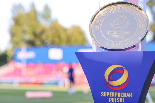 Złote trofeum za zdobycie Superpucharu Polski umieszczone na niebieskim podeście na tle stadionu piłkarskiego