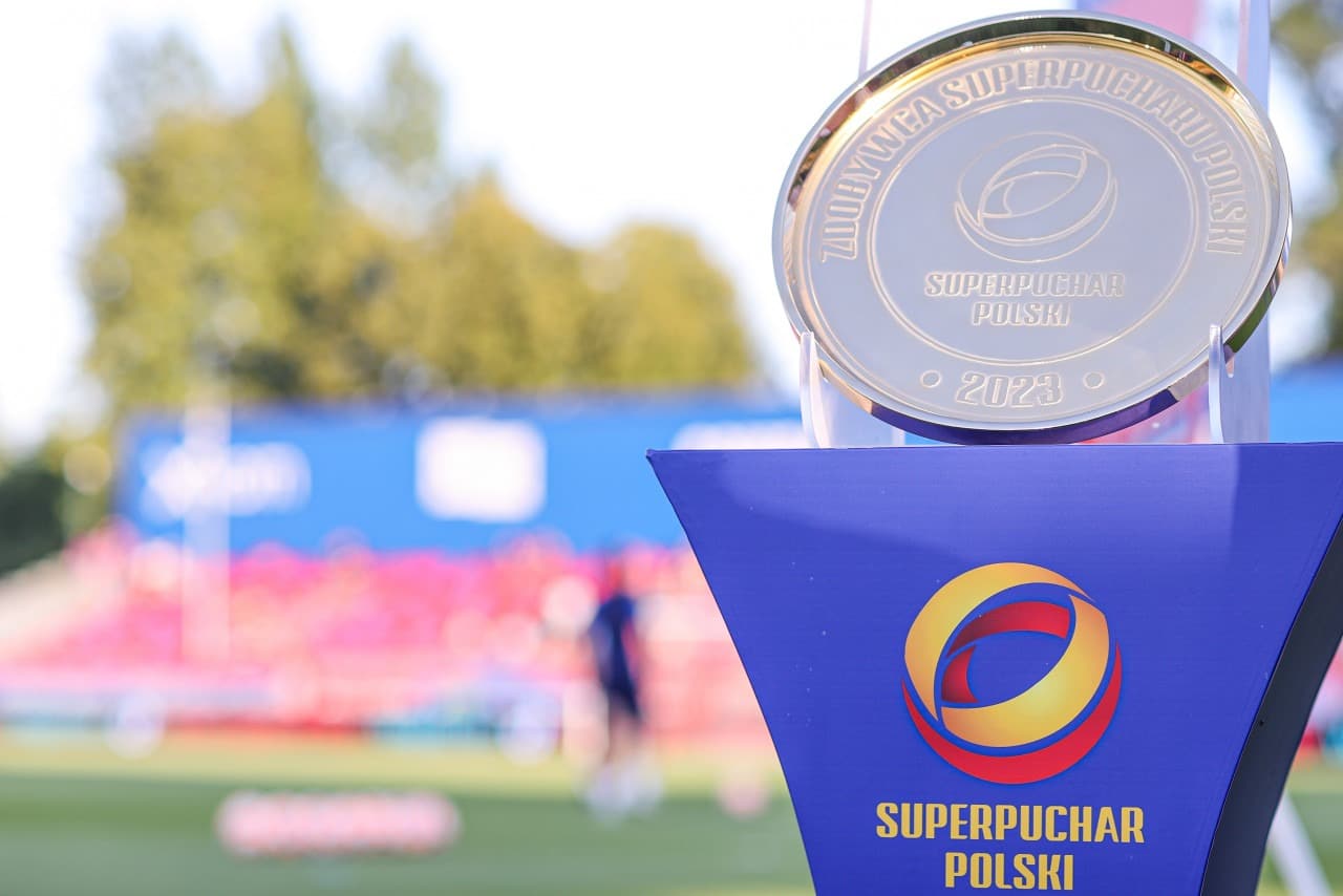 Złote trofeum za zdobycie Superpucharu Polski umieszczone na niebieskim podeście na tle stadionu piłkarskiego