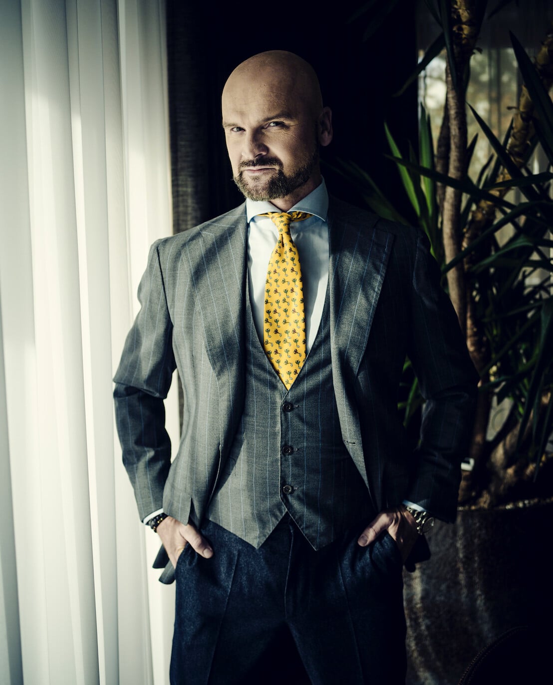 Rafał Brzoska, założyciel i prezes InPostu, ubrany w szary garnitur, kamizelkę i żółty krawat, stojący przy oknie.